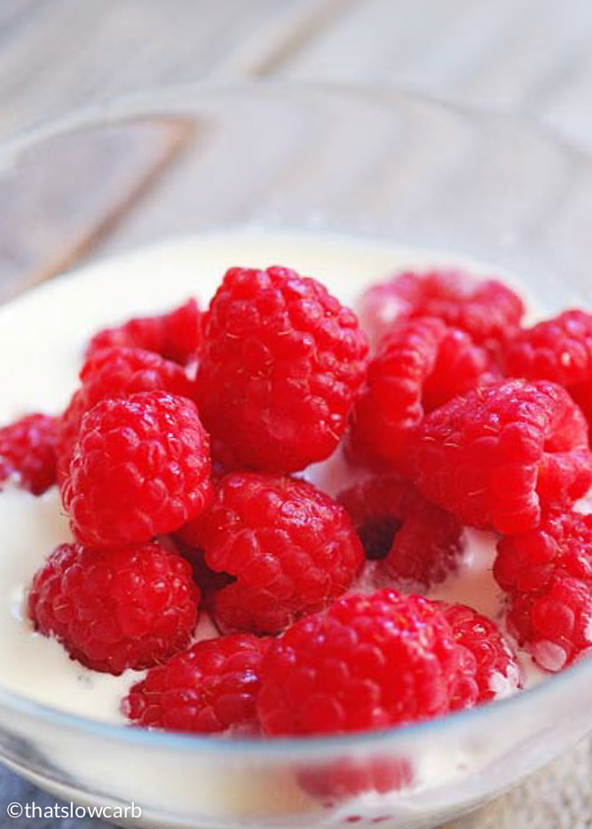 Low Carb Berries and Cream Raspberries sitting in cream in clear bowl