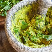 Low Carb Guacamole mixed in a mortar and pestle bowl beside cilantro.