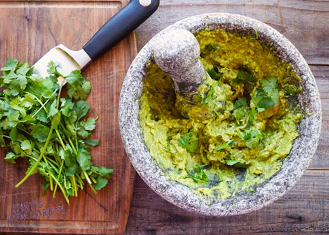 Overhead shot of Low Carb Guacamole mixed in a mortar and pestle bowl beside cilantro.