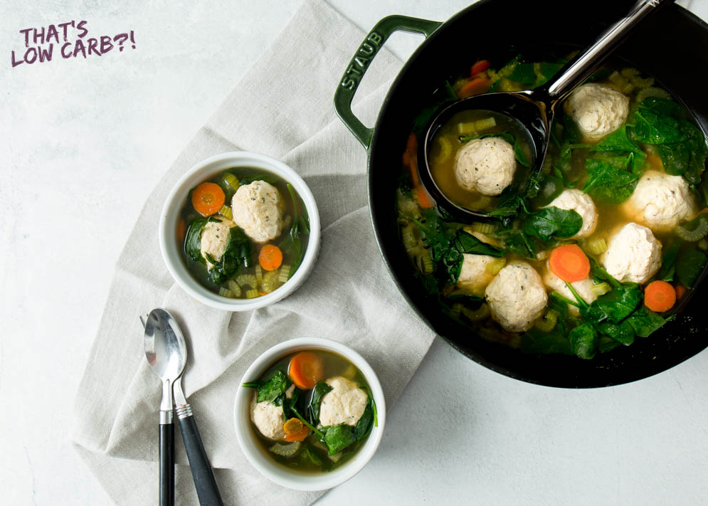 Overhead shot of Keto Low Carb Italian Wedding Soup in two small white bowls and a black pot with a black ladle with a black handle spoon and fork laying beside.