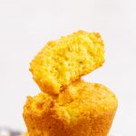Low Carb Cornbread Muffins Stacked with the top muffin cut in half in front of white background