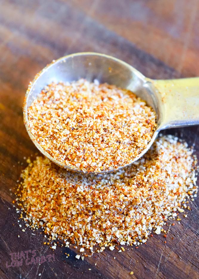 Low carb taco seasoning in tablespoon overflowing onto wood board.