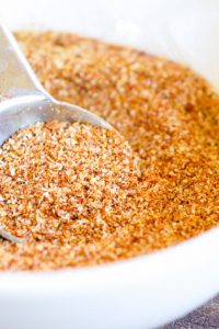 The Best Low Carb Taco Seasoning in a white bowl being scooped up by a tablespoon.