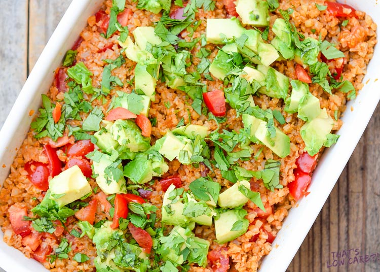 Image of keto Mexican Cauliflower Rice with green garnish and avocado on top in a white casserole dish.