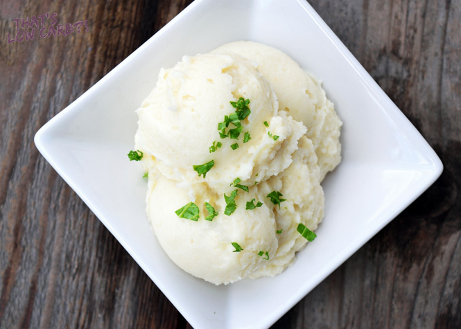 Close up overhead shot of keto cauliflower mashed potatoes in a white square bowl with green garnish sprinkled on top.