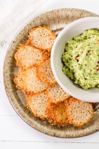 Overhead shot of Low Carb, keto Cheese Chips on a plate next to a bowl of guacamole.