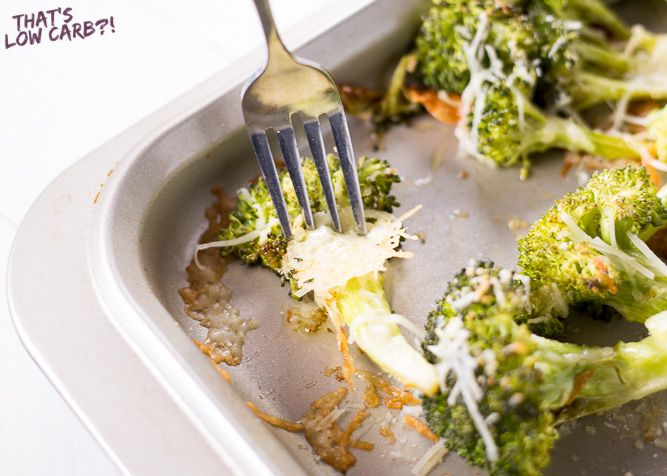 Oven Roasted Low Carb Broccoli on a baking sheet with cheese sprinkled over top and one being lifted by a fork.