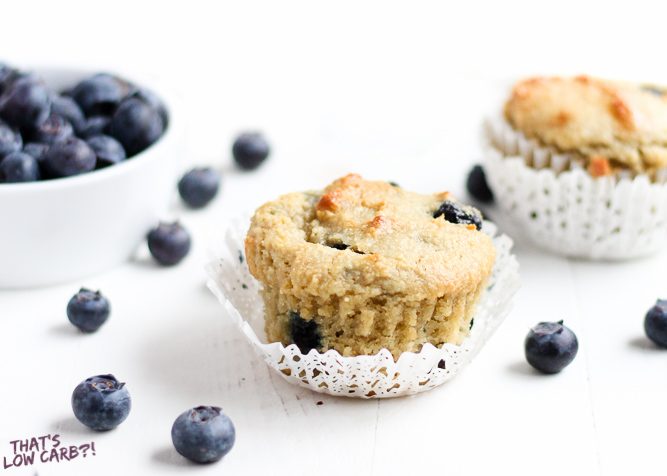 Low Carb Blueberry Muffins with blueberries spread around and a bowl of blueberries beside.
