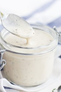 Image of Keto Low Carb Ranch Dressing in a glass jar with a spoon full being lifted out.
