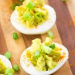 Image of keto Low Carb Deviled Eggs with green onions on a wood cutting board.
