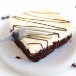 Image of Low Carb Cheesecake Brownie square with white frosting and chocolate drizzle being sliced by a fork.