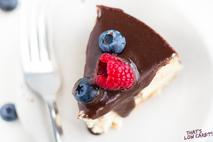 Image of of Keto Cheesecake slice with chocolate sauce over top and raspberry and blueberry.