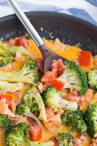 Image of Sundried Tomato Keto Salmon Dinner in a skillet with tomato and broccoli and orange sauce with large spoon scooping some.