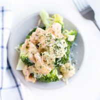 Overhead shot of Low Carb Smoked Salmon Cream Cheese Sauce over broccoli with Parmesan cheese sprinkled on top on a white plate.