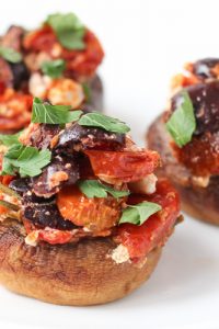 Image of three Low Carb keto Stuffed Mushrooms with olives, tomato. and feta on a white plate.