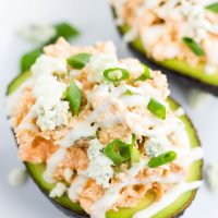 Image of two Image of Low Carb Buffalo Chicken Stuffed Avocado on a white plate and green onion sprinkled on top.