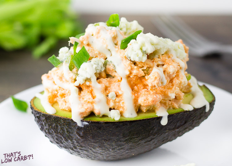 Close up shot of Low Carb Buffalo Chicken Stuffed Avocado on a white plate and green onion sprinkled on top.
