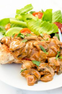 Image of Keto Fat Bomb Chicken with sauce and mushrooms and a side salad on a white plate.