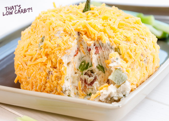 Image o keto Pumpkin Cheese Dip pumpkin shaped cheese ball with a small portion missing showing the inside on a small baking sheet.