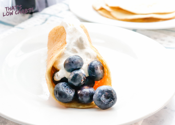 Image of Easy Low Carb Keto Crepes filled with blueberries and whipped cream on a white plate.