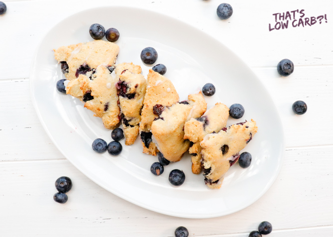 Overhead shot of Low Carb Scones in a line on a oval white plate with blueberries sprinkled around.