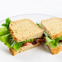 Image of keto bread sandwich sliced in half with lettuce and bacon showing on a white plate.