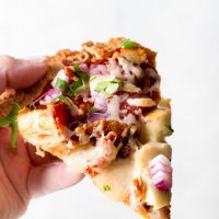 Image of Keto BBQ Chicken Pizza being held in one hand with white background.