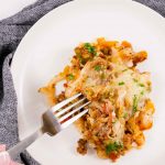 Image of keto cabbage roll casserole portion on a white plate with a silver fork held over on top of a grey tea towel.