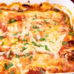image of keto lasagna in a white pan with green garnish sprinkled on top. Blurred image of a red tea towel in the upper right corner in the background.