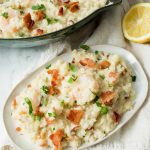 Image of Low Carb Keto Cauliflower Risotto with bacon and green garnish sprinkled on top on a white plate with a fork sticking out. A partial image of a black bowl with Low Carb Keto Cauliflower Risotto above.