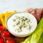 Bowl of Blue Cheese Dressing surrounded by lettuce, tomatoes, peppers and prosciutto