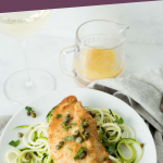 chicken piccata on top of zucchini noodles on a white plate